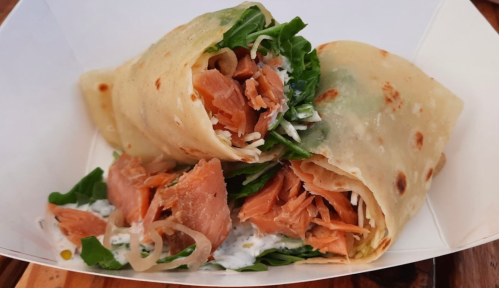 A close-up of a wrap filled with salmon, lettuce, and sauce, served in a white paper container.