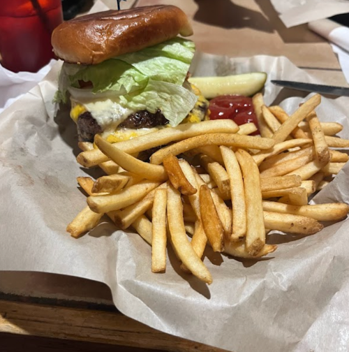 A juicy cheeseburger with lettuce on a bun, served with a side of golden fries and a pickle, on a paper-lined plate.