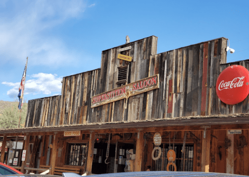 Exterior of Superstition Saloon with wooden facade, Coca-Cola sign, and American flag under a blue sky.