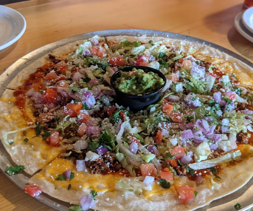 A large pizza topped with guacamole, lettuce, tomatoes, onions, and cheese on a wooden table.