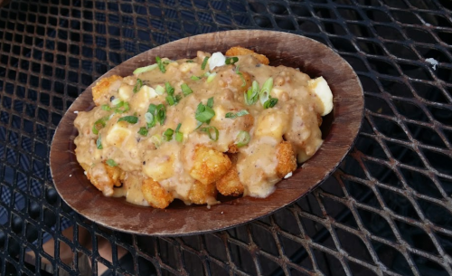 A wooden bowl filled with tater tots topped with gravy and chopped green onions.