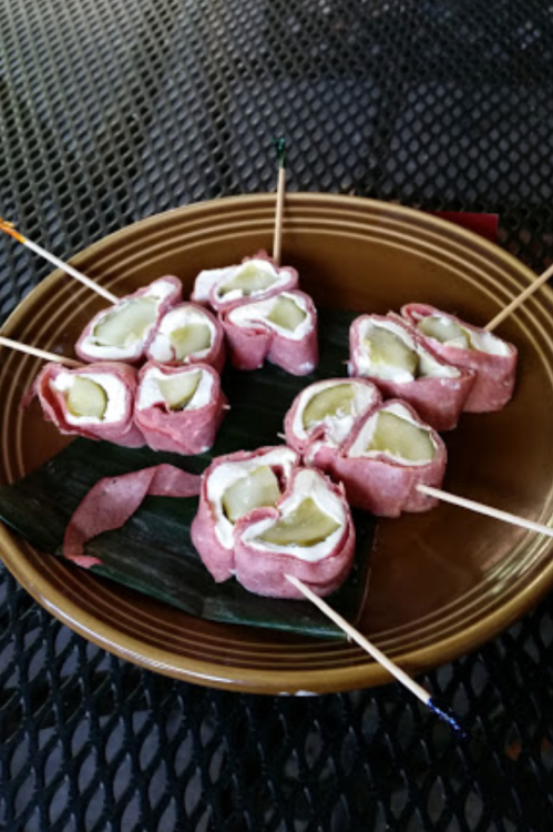 A plate of rolled sushi with pickles, wrapped in meat and secured with toothpicks, resting on banana leaves.