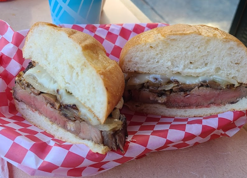 A close-up of a sandwich with layers of meat and melted cheese, served on a soft bun with a checkered paper lining.