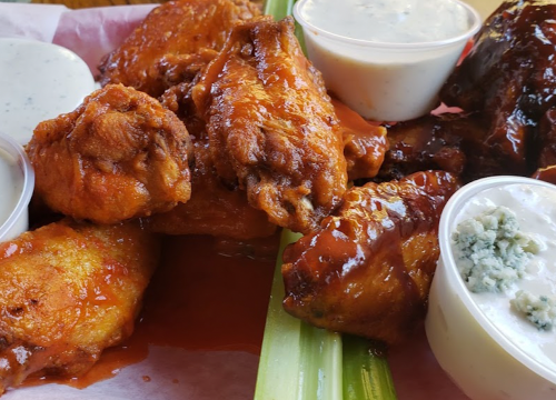 A platter of crispy chicken wings with two dipping sauces and celery sticks on a red paper-lined tray.
