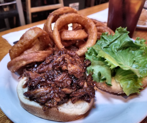 A plate featuring a pulled pork sandwich with lettuce, surrounded by crispy onion rings.