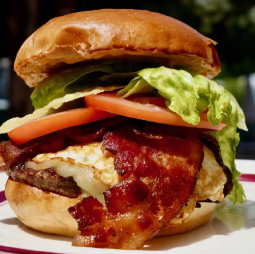 A close-up of a burger with bacon, lettuce, tomato, and a fried egg on a toasted bun.