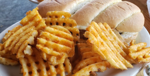 A plate with a sandwich and a generous serving of crispy waffle fries.