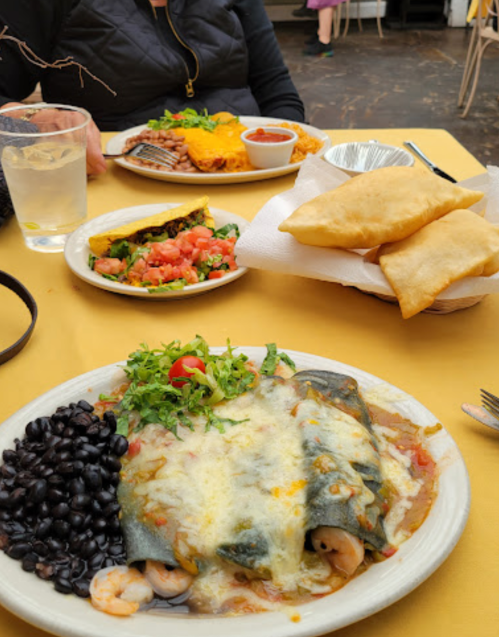 A plate of enchiladas topped with cheese, black beans, a side salad, and crispy pastries on a yellow tablecloth.