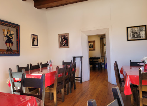 Cozy restaurant interior with wooden tables, red tablecloths, and framed photos on the walls.