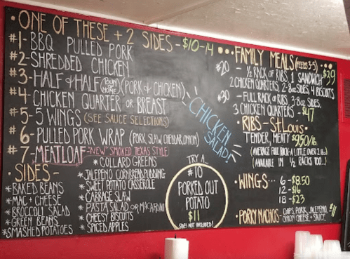 Chalkboard menu featuring BBQ dishes, sides, family meals, and prices for pulled pork, chicken, ribs, and more.