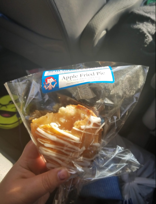 A hand holding a partially eaten apple fried pie in a clear bag, with a label on it.