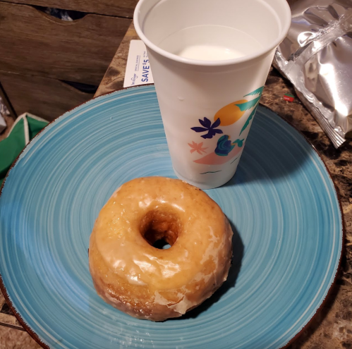 A glazed donut on a blue plate next to a white cup filled with milk.