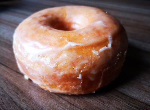 A glazed donut resting on a wooden surface, showcasing its golden-brown color and shiny icing.