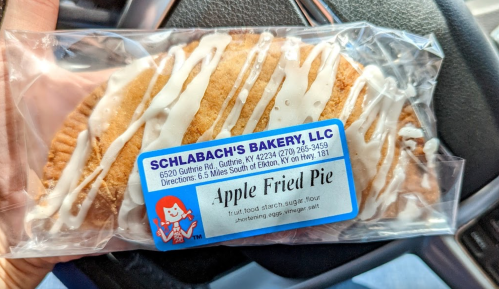 A packaged apple fried pie from Schlabach's Bakery, with a white icing drizzle on top, resting in a car.