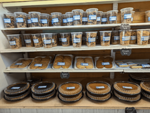 Shelves filled with jars of granola, cookies, and pies, all labeled with prices.