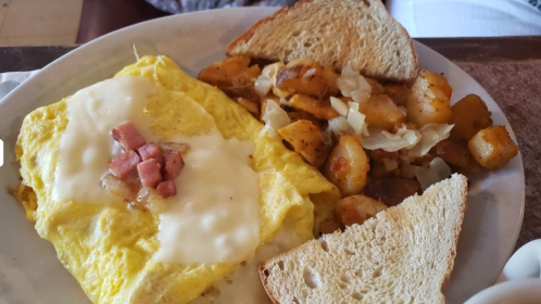 A plate with an omelette topped with ham and cheese, served with seasoned potatoes and two slices of toast.