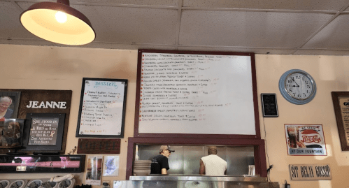 A diner interior featuring a menu board, clock, and two cooks working behind the counter.