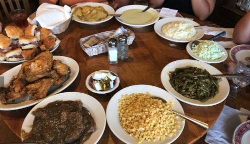 A table spread with various dishes, including fried chicken, green beans, corn, mashed potatoes, and biscuits.