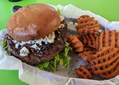 A juicy burger with blue cheese and lettuce, served with a side of crispy waffle fries on a green table.