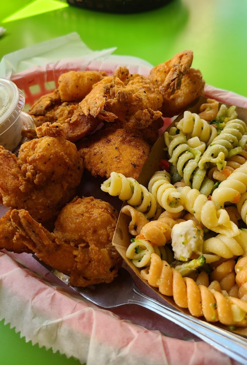 A tray with fried shrimp, chicken, and a side of pasta salad on a bright green table.