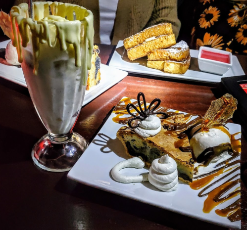 A dessert spread featuring a tall milkshake, a slice of cake with caramel, and whipped cream on a plate.