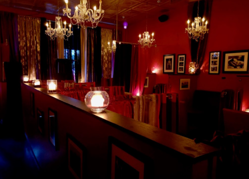 Cozy interior of a dimly lit room with chandeliers, candles, and rich red decor, creating an intimate atmosphere.