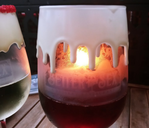 A close-up of a glass with a dripping white topping, revealing a glowing light inside and a dark beverage below.
