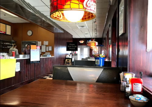 A cozy diner interior with a wooden table, colorful light fixture, and a gumball machine in the background.