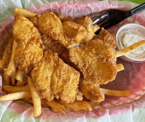 A basket of crispy fried chicken tenders served with French fries and a side of dipping sauce.