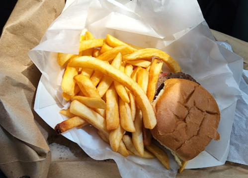 A burger in a bun with a side of golden French fries, served in a paper container.
