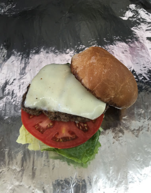 A hamburger with a beef patty, melted cheese, tomato slices, and lettuce on a bun, resting on shiny foil.