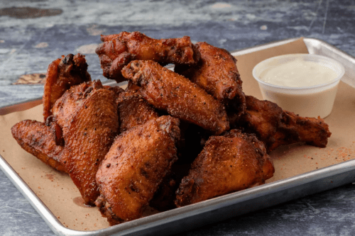 A platter of crispy fried chicken wings served with a small cup of dipping sauce.