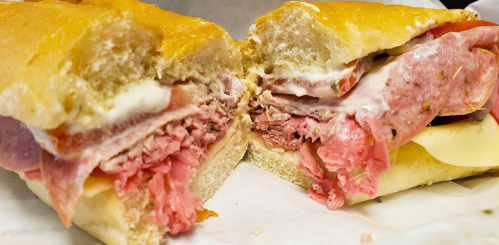 A close-up of a freshly cut sandwich filled with layers of meats, cheese, and mayonnaise on a soft hoagie roll.