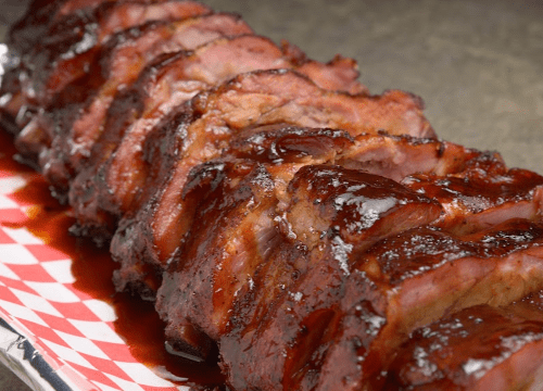 Sliced barbecue meat glazed with sauce, arranged neatly on a checkered platter.