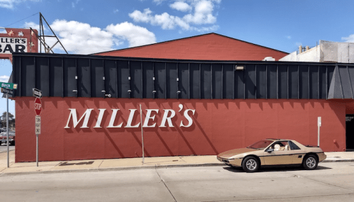 A gold car parked beside a red building with "MILLER'S" written in large white letters on the wall.