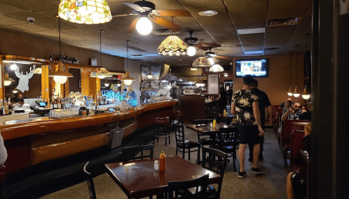 A cozy restaurant interior with stained glass lamps, a bar, and patrons dining at tables.