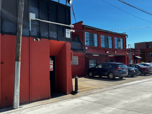 A red building with a parking lot, featuring a sign and a clear blue sky above.
