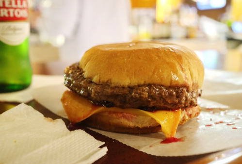 A close-up of a juicy hamburger with melted cheese and ketchup on a soft bun, resting on a napkin.