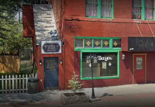 A red brick building with a sign for "Old Bakery Hotel" and a green window labeled "Bayou," featuring a decorative lamppost.