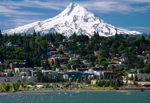 A scenic view of a snow-capped mountain towering over a lush green landscape and a vibrant waterfront community.
