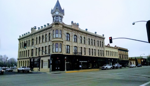 Historic building with a clock tower, featuring ornate architecture, located at a street intersection on a cloudy day.