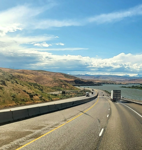 A winding highway alongside a river, with hills and blue skies in the background.