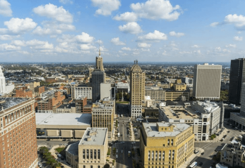 Aerial view of a city skyline featuring various buildings and a clear blue sky with scattered clouds.