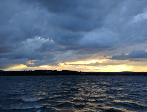 A serene seascape at sunset, with dark clouds and gentle waves reflecting the warm hues of the fading light.