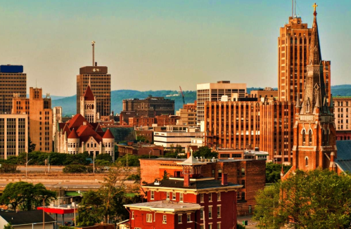 A city skyline featuring modern buildings and a historic church steeple against a clear sky.