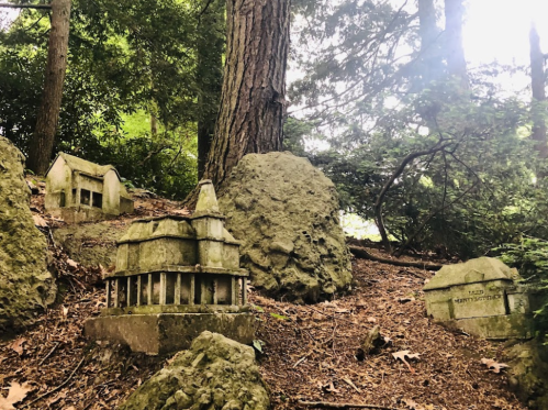 Miniature stone structures nestled among rocks and trees in a wooded area.