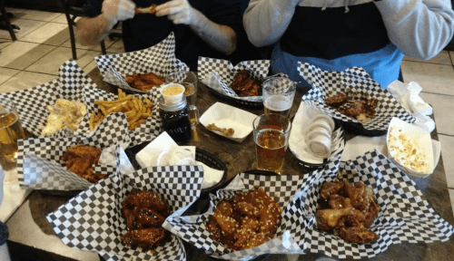 A table filled with various chicken wings, fries, and drinks, all served in checkered paper baskets.