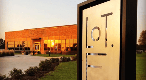 A modern brick building at sunset, featuring a sign that reads "LoT." in front of a landscaped area.