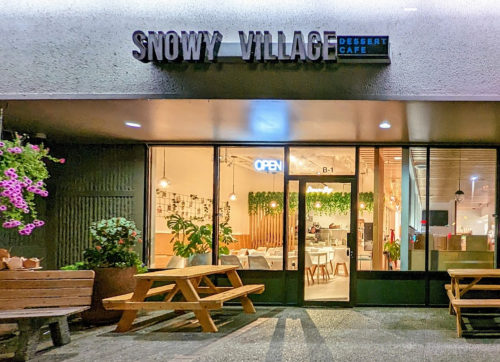 Exterior of Snowy Village Dessert Café, featuring an open sign, outdoor seating, and vibrant plants.