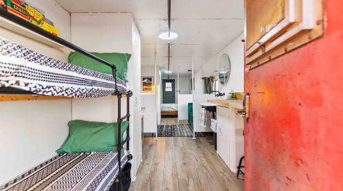 Interior of a small, modern space featuring bunk beds, a kitchenette, and a bathroom area with wooden flooring.